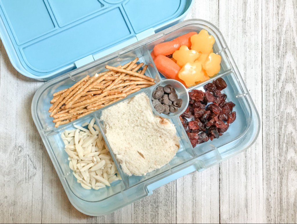 Chocolate chips, dried cranberries and almonds with sandwich, bell peppers, and pretzel sticks for a kid's lunch in a Yumbox bento lunchbox