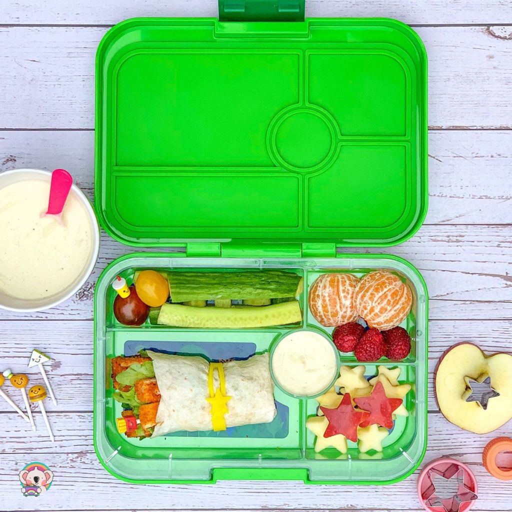 Yogurt in the round compartment of a Yumbox for a kid to dip its cucumber sticks into