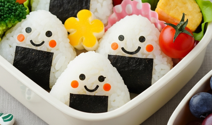 A colorful kids’ lunchbox with traditional triangular onigiri, veggie sides, and bento-style presentation.