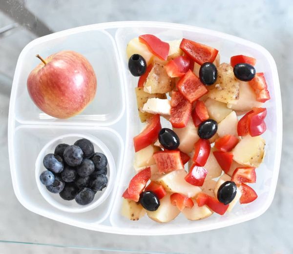 A patriotic Independence Day lunchbox featuring a creamy potato salad with red bell peppers and black olives, served alongside red apple slices and juicy blueberries. This red, white, and blue lunch is both refreshing and kid-friendly, perfect for July 4th celebrations, school lunches, or picnics. Explore more holiday lunchbox ideas at Teuko.com.