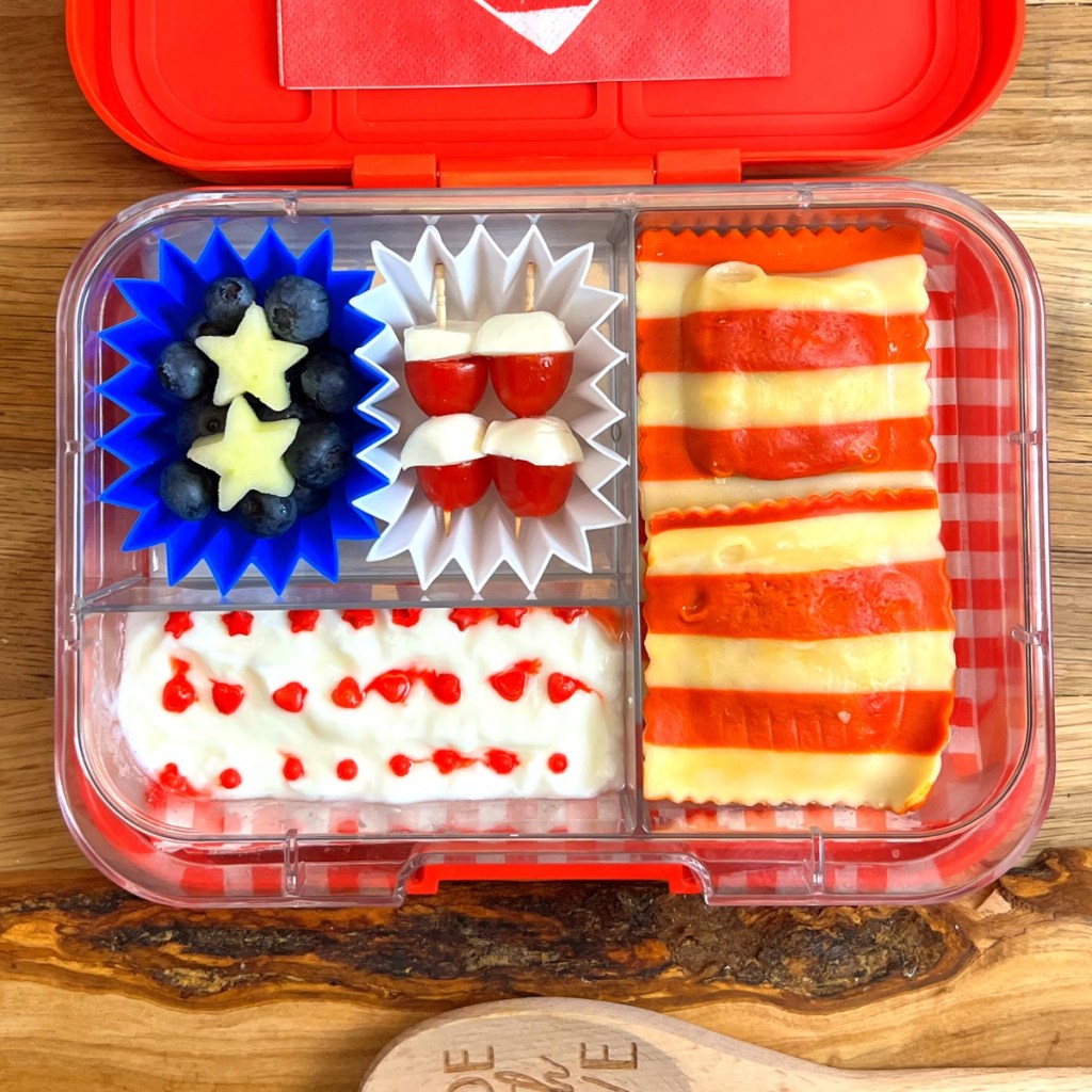 A festive kids' lunchbox inspired by Independence Day, featuring red and white striped pasta, mozzarella and cherry tomato skewers, and fresh blueberries. This colorful, patriotic lunch is perfect for July 4th celebrations or any summer picnic. Easy to pack, fun to eat, and guaranteed to spark joy. Discover more creative holiday lunchbox ideas at Teuko.com.