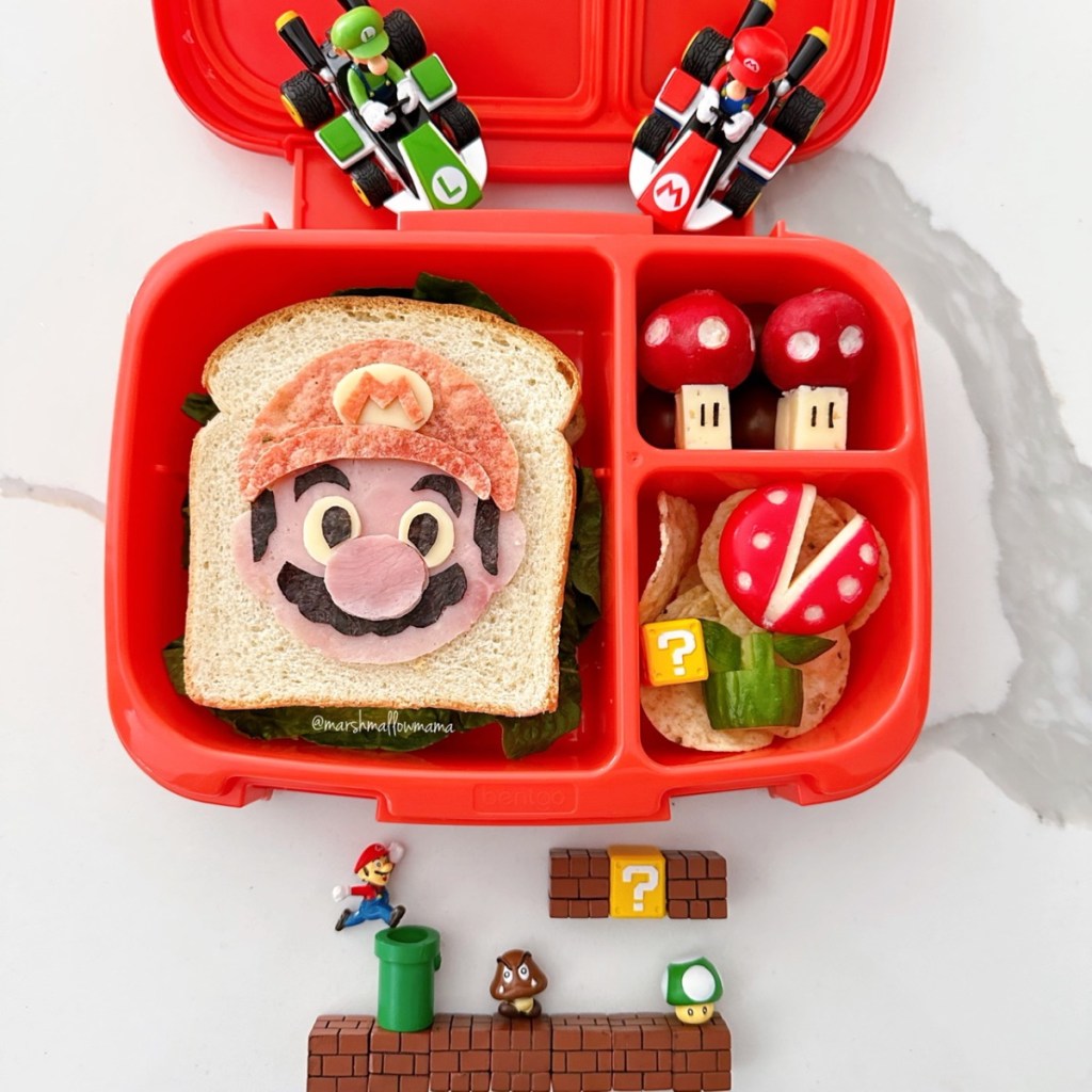 Super Mario-themed kids’ lunchbox featuring a red and white Toad-inspired radish alongside a sandwich and a cool Babybel monster plant for a playful and healthy school meal.