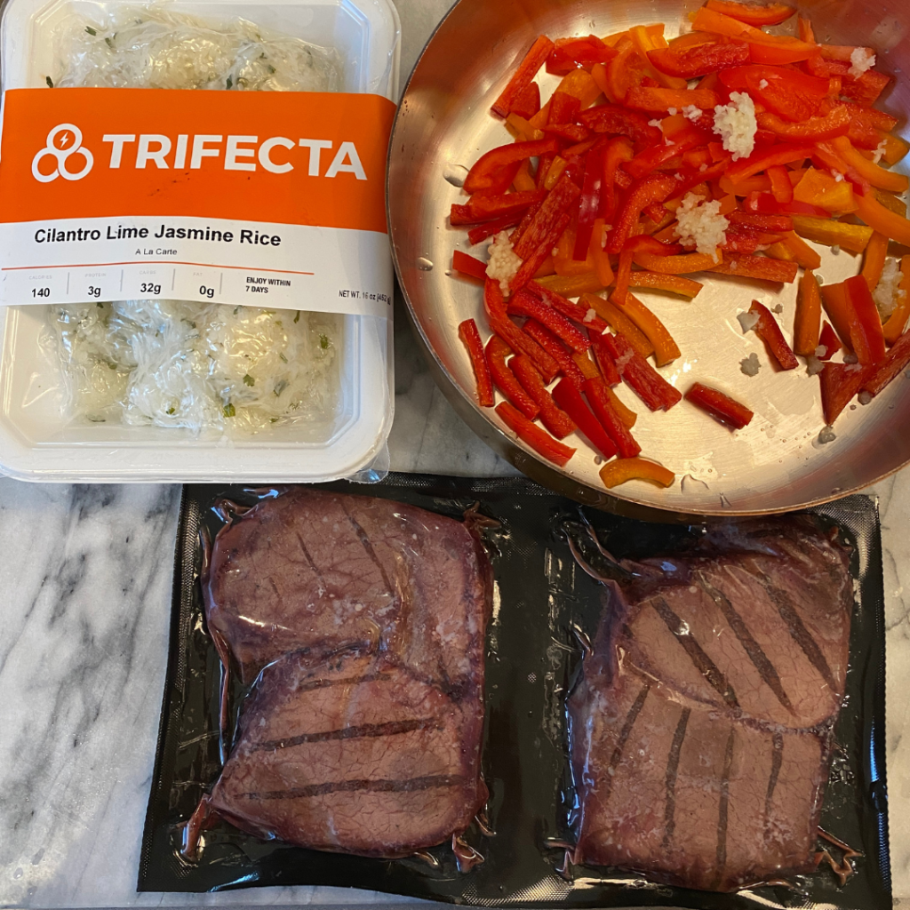 Trifecta meal prep with cilantro lime rice, seasoned beef steaks, and fresh vegetables packed in a  lunchbox for kids and teens school lunch by Teuko.