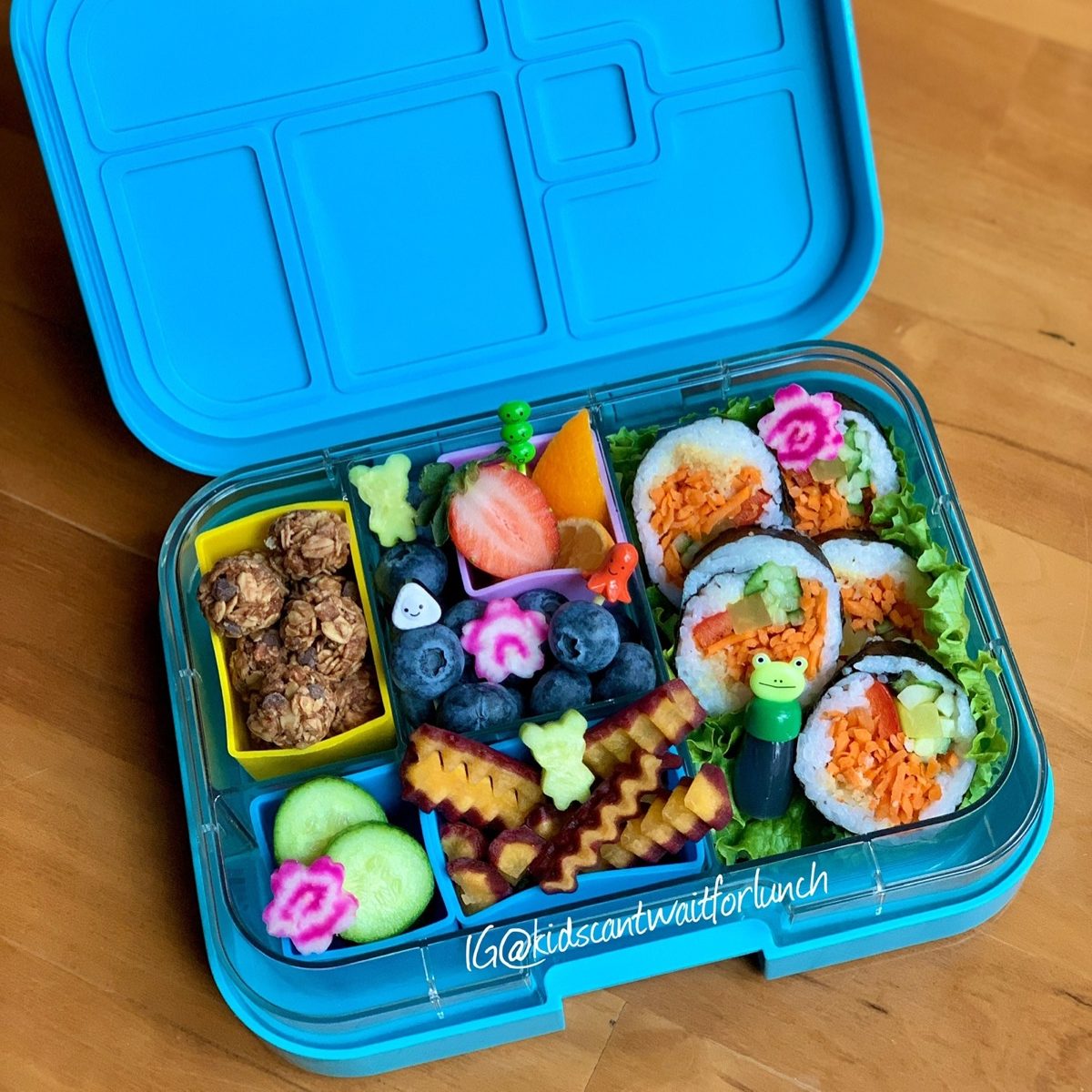 Veggie sushi and colorful vegetables and fruits in a blue lunchbox for kids