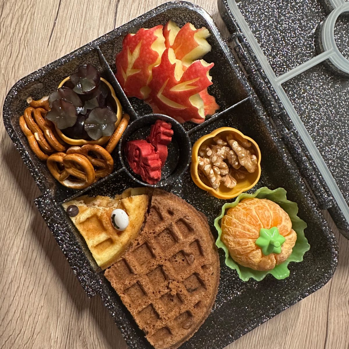 A kids lunchbox that has leaves-shaped apples and a Hedgehog waffle.