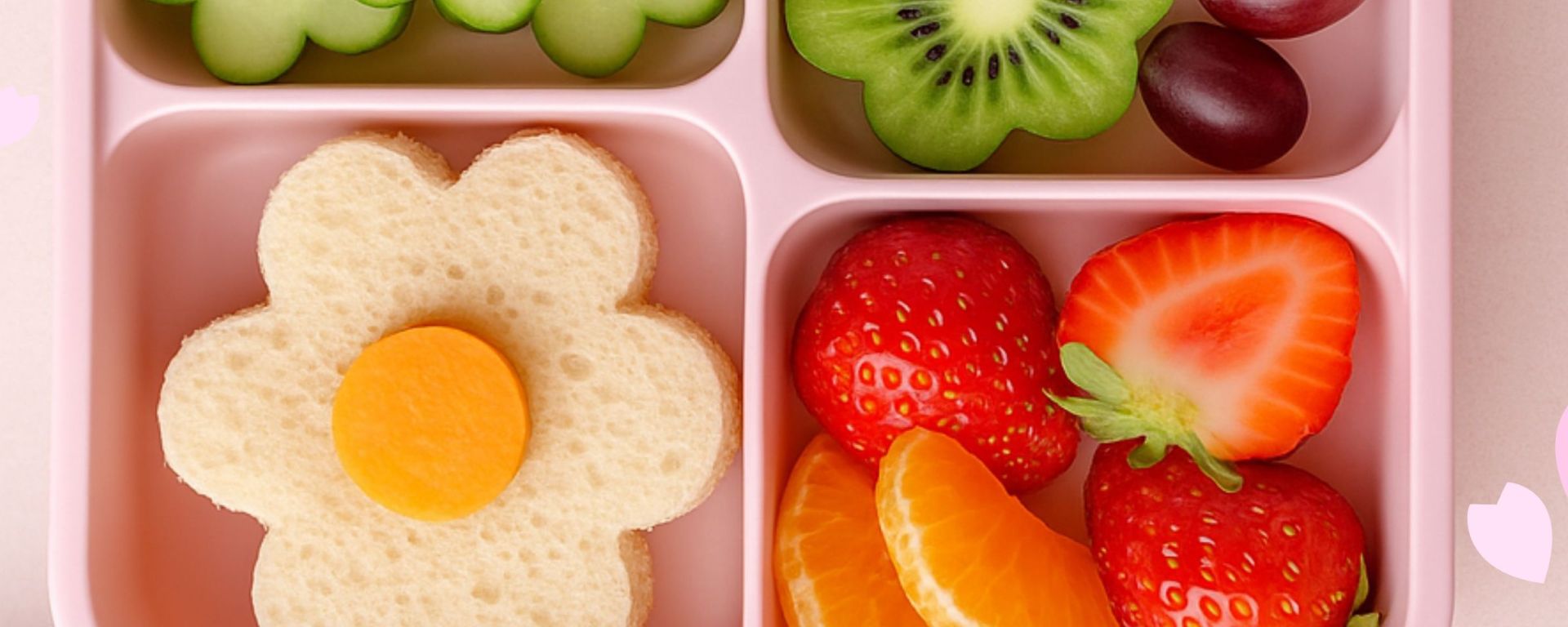 Spring-themed lunchbox with a flower-shaped sandwich, cucumber slices arranged as flowers, kiwi flower, strawberries, mandarin slices, and grapes in a pastel bento box.