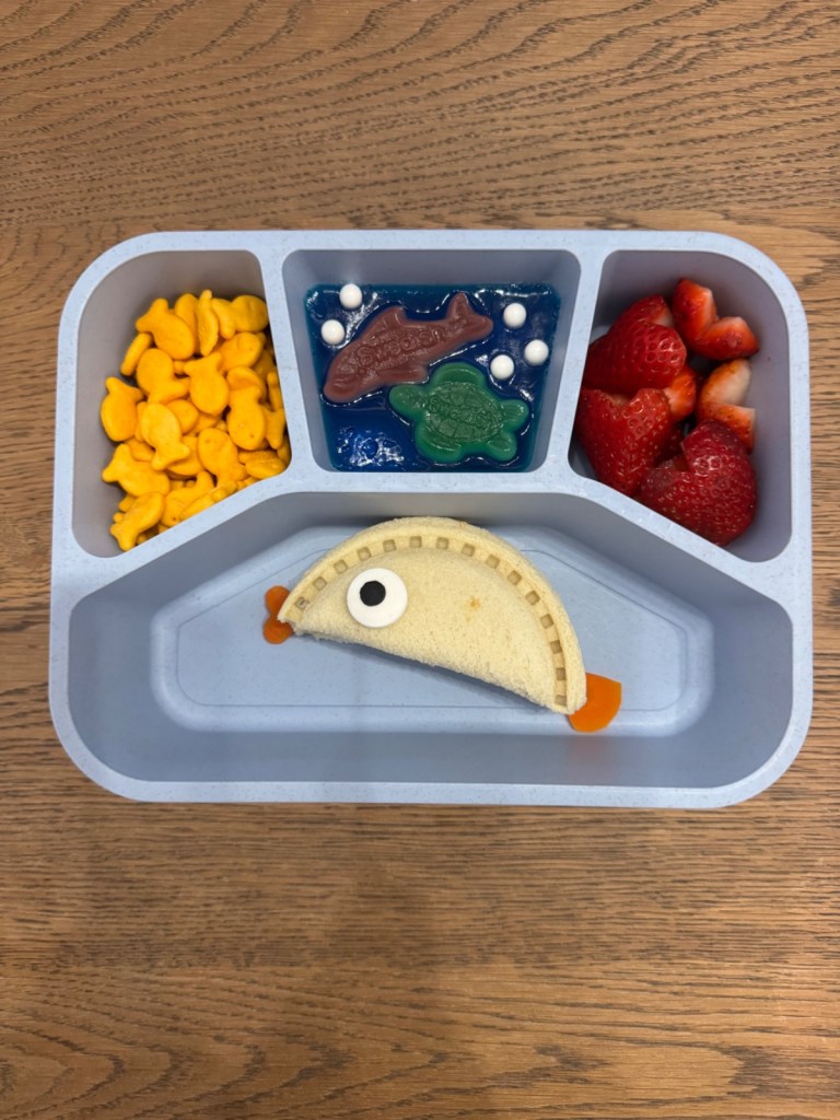 Ocean-themed lunchbox idea for a kid with fish crackers, fish-shaped sandwich, and blue "ocean" jelly