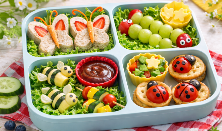 Nature-themed lunchbox with butterfly sandwiches, caterpillar fruit skewers, ladybug crackers, and bee-shaped cheese rolls in bright natural light.