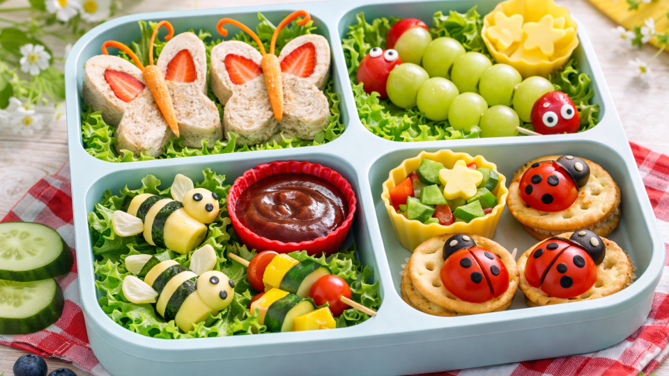 Nature-themed lunchbox with butterfly sandwiches, caterpillar fruit skewers, ladybug crackers, and bee-shaped cheese rolls in bright natural light.