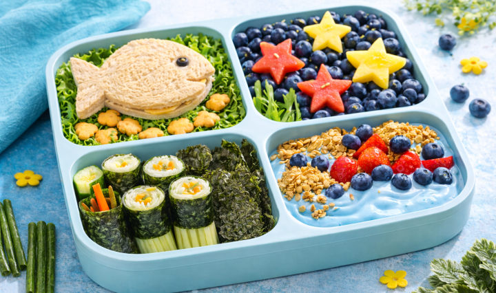 Ocean-themed lunchbox with fish-shaped sandwich, blueberry ocean, seaweed snacks, and star-shaped fruit in bright natural light.